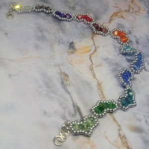 May include: A rainbow-coloured beaded bracelet with silver accents. The beads are arranged in a zig-zag pattern and are connected by silver wire.