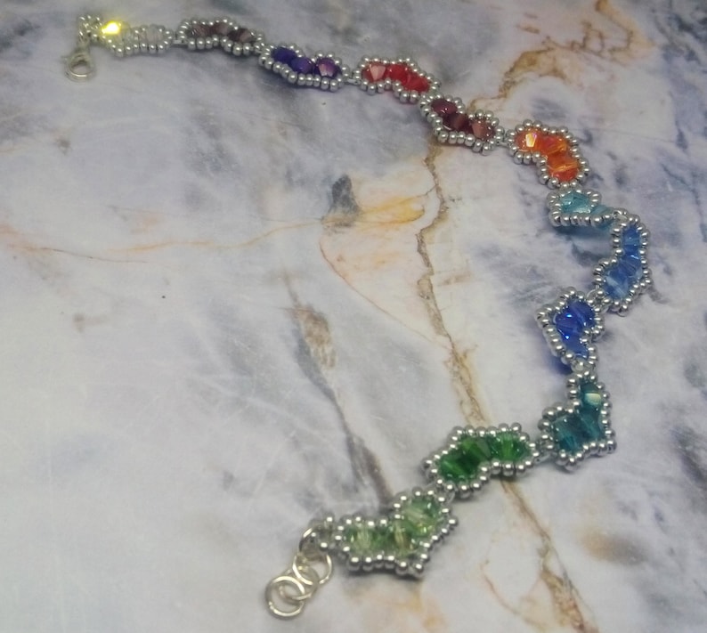 May include: A rainbow-coloured beaded bracelet with silver accents. The beads are arranged in a zig-zag pattern and are connected by silver wire.