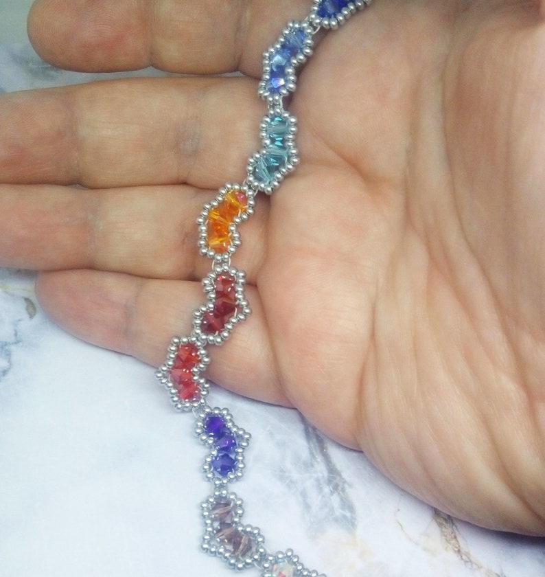 May include: A rainbow-coloured beaded necklace with silver accents. The beads are arranged in a zig-zag pattern.