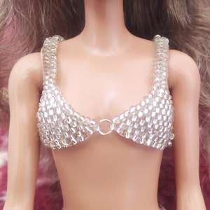 May include: A silver beaded bra top with a ring closure in the center. The bra top is made of small, clear beads.