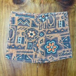 May include: Brown and orange patterned shorts with a repeating design of flowers, geometric shapes, and lines. The shorts have a high waist and a classic fit. The fabric appears to be a woven material.