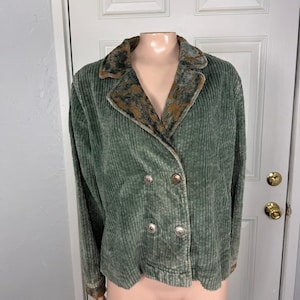 May include: A sage green corduroy jacket featuring a double-breasted front with four metallic buttons. The jacket has a notched collar with a contrasting brown and black patterned fabric trim that matches the cuffs on the long sleeves.