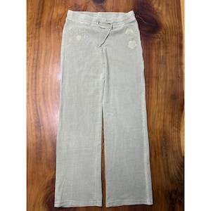 May include: Light green velour sweatpants with a drawstring waist and embroidered floral details. The pants have a wide leg design and are made of a soft, comfortable material. The pants are shown on a wooden surface.