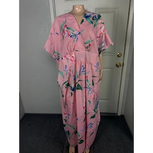 May include: A floor-length pink kaftan dress featuring a V-neckline and short sleeves. The garment is decorated with a repeating floral pattern in shades of blue, purple, and green, with a defined waistline and a loose, flowing silhouette.
