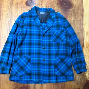 May include: A blue and black plaid blazer with two front pockets and three buttons. The blazer has a notched collar and a black lining. The fabric appears to be a soft wool or wool blend.