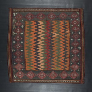 May include: A traditional rug with a geometric pattern in shades of red, orange, green, and black. The rug has a dark brown border with a repeating design.