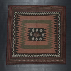 May include: A square woven rug with a geometric pattern in shades of brown, black, and green. The rug has a central diamond shape with smaller diamonds around it.