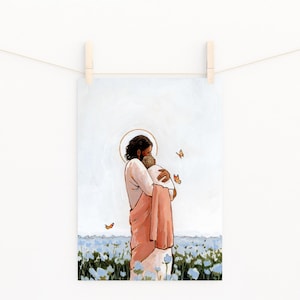 Op de afbeelding: Een kunstdruk met een figuur in een perzikkleurige jurk die een andere figuur omhelst, beide met halo's. De achtergrond toont een veld met blauwe bloemen en oranje vlinders. De print hangt aan een waslijn met houten wasknijpers.