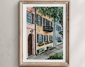 May include: Watercolor painting of a row of colorful houses with a balcony and a wrought iron railing. The houses have black shutters and windows. The painting is framed in a light wood frame.
