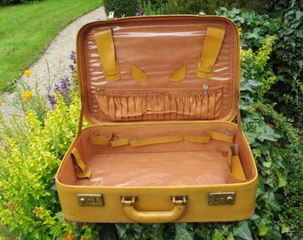 Op de afbeelding: Een vintage gele koffer met een bruin interieur en meerdere compartimenten. De koffer heeft een metalen sluiting en een handvat.
