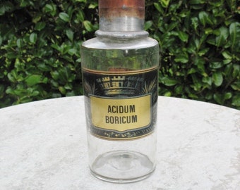 May include: A clear glass bottle with a copper top and a black and gold label that reads "Acidum Boricum".