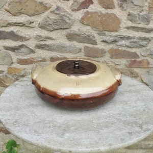 May include: A brown and beige ceramic pot with a lid. The pot has a rounded shape and a brown rim. The lid is brown and has a knob on top.