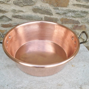 May include: A large copper pot with two handles. The pot is sitting on a light gray stone surface.