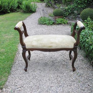 Puede incluir: Banco antiguo con asiento tapizado verde claro y estructura de madera marrón oscuro. El banco tiene brazos y patas curvadas y está colocado sobre un camino de grava en un jardín. Es un mueble clásico.