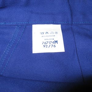 May include: A blue fabric label with white text. The label includes washing instructions, fabric content, and size information. The text reads: "35% POLYESTER 65% COTON 767174M 92/76"