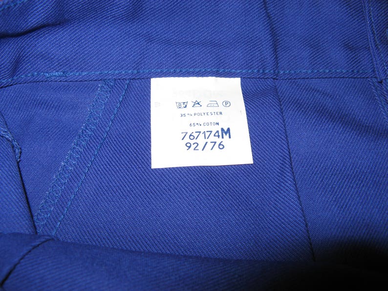 May include: A blue fabric label with white text. The label includes washing instructions, fabric content, and size information. The text reads: "35% POLYESTER 65% COTON 767174M 92/76"