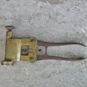 May include: A vintage brass wire cutter with a lever handle and a metal frame. The cutter has a label that reads "Made in Sweden".