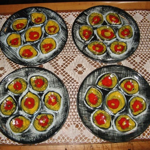 May include: Set of four black ceramic oyster plates with yellow and red accents. Each plate has six individual indentations for serving oysters.
