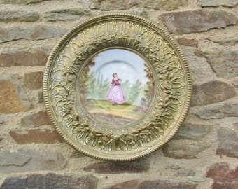 Una placa colgante de pared de latón europeo vintage muy bonita con placa central de porcelana pintada de una niña en una escena de paisaje