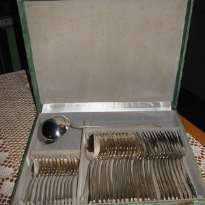 May include: A green velvet-lined box containing a set of silverware. The silverware includes forks, spoons, and a ladle. The box is open and the silverware is arranged neatly inside.