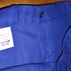 May include: A close-up of a blue pair of work pants with a white label that says "767174M 92/76".