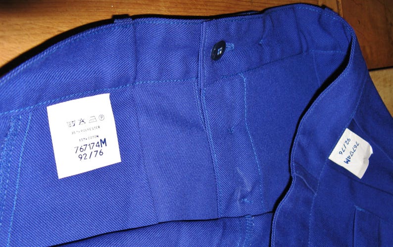 May include: A close-up of a blue pair of work pants with a white label that says "767174M 92/76".
