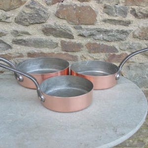 Een gegradueerde set van drie vintage Franse koperen braadpannen/braadpannen met ijzeren handgrepen