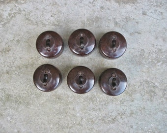 May include: Seven vintage brown bakelite light switch covers with a black toggle switch in the center of each.
