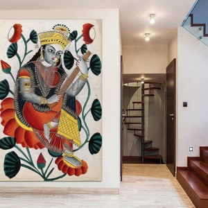May include: A framed artwork depicting a seated figure playing a stringed instrument, surrounded by red and green floral elements. The figure is adorned in traditional attire with gold accents, set against a neutral background.