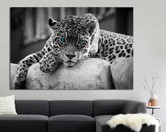 May include: A black and white photograph of a jaguar with bright blue eyes. The jaguar is lying on a rock with its head resting on its paws.