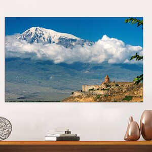 May include: A scenic photograph of a mountain range with a church on a hilltop. The mountain is covered in snow and clouds. The church is a red brick building with a white dome. The sky is blue and the clouds are white.