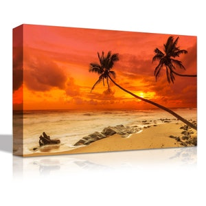 May include: A vibrant orange and red sunset over a tropical beach with two palm trees silhouetted against the sky. The beach is sandy with rocks and a piece of driftwood in the foreground.