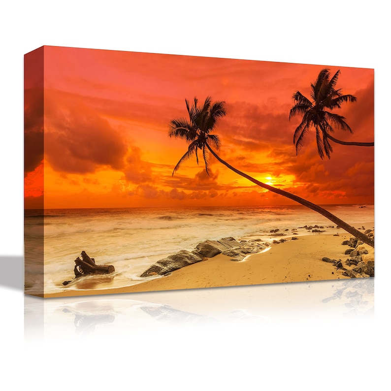 May include: A vibrant orange and red sunset over a tropical beach with two palm trees silhouetted against the sky. The beach is sandy with rocks and a piece of driftwood in the foreground.