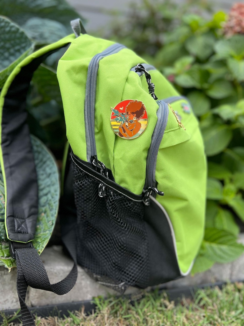 May include: A green backpack with a black mesh pocket and a gold pin featuring a cartoon character with a red afro and a yellow background.