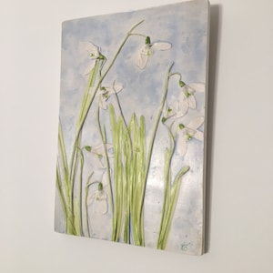 May include: A ceramic wall art piece depicting a cluster of white snowdrop flowers with green stems against a light blue background.