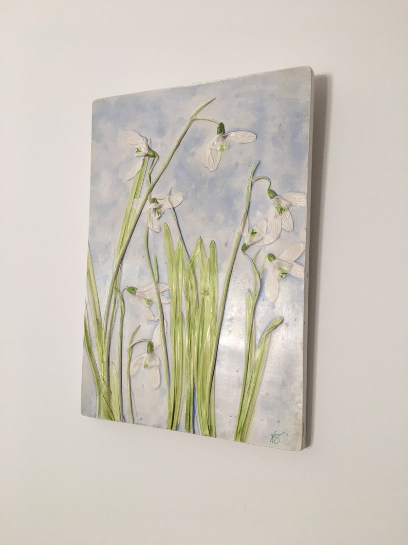 May include: A ceramic wall art piece depicting a cluster of white snowdrop flowers with green stems against a light blue background.