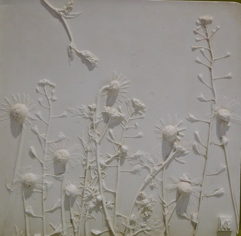 May include: White plaster relief sculpture of a group of wild flowers, including daisies and other delicate blooms. The flowers are arranged in a natural, flowing pattern, creating a sense of movement and life. The sculpture is a beautiful and unique piece of art that would add a touch of nature to any home.
