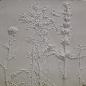 May include: A white plaster relief sculpture of three different types of plants. The plants are arranged in a vertical composition, with the tallest plant on the right side of the image. The plants are all in a natural, organic style, with delicate details.