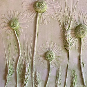 Op de afbeelding: Een witte achtergrond met een 3D-reliëfdesign van witte madeliefjes en groene tarwehalmen.