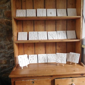 May include: A wooden cabinet with two drawers and three shelves. The shelves are filled with white ceramic tiles with raised floral designs.