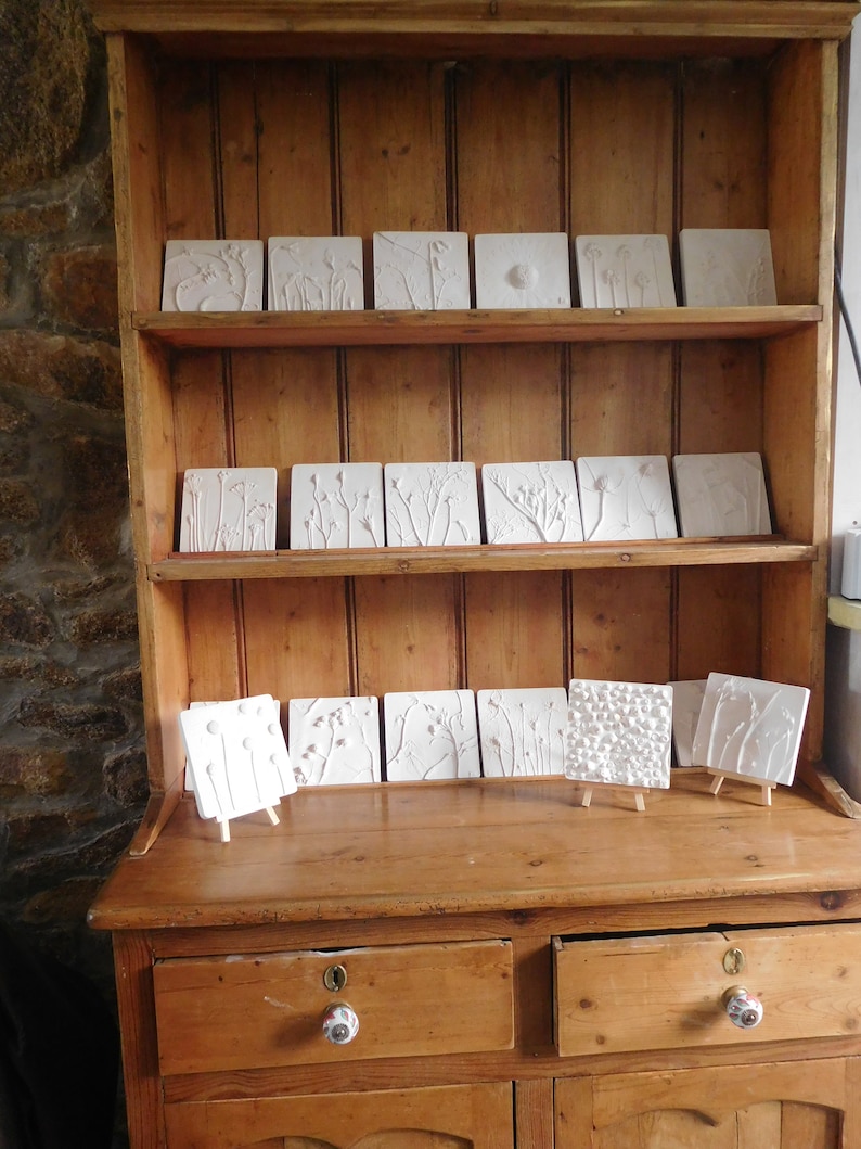 May include: A wooden cabinet with two drawers and three shelves. The shelves are filled with white ceramic tiles with raised floral designs.
