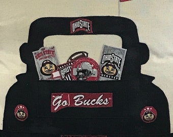 May include: A decorative pillow featuring a black truck silhouette filled with Ohio State Buckeyes memorabilia. The truck bed displays a football, helmet, and various logo items. A pennant with the Ohio State logo flies above, and the words "Go Bucks" are prominently displayed.
