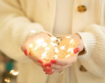 May include: A person's hands holding a string of white fairy lights with star-shaped bulbs. The lights are glowing and creating a warm, festive atmosphere.