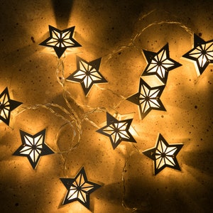 May include: A string of white star-shaped lights with a warm glow. The lights are strung together with clear wire and are perfect for adding a festive touch to any space.