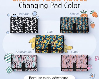 May include: Five rectangular foldable changing pads with black trim and center straps. Patterns include black and white pandas, blue and green berries, yellow and blue fruits, pink and black abstract lines, and pink and black cat silhouettes.