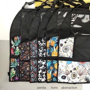 May include: Six black fabric organizers with clear plastic windows and multiple pockets. The organizers have different colorful patterns, including tropical leaves, geometric designs, pandas, lions, and abstract flowers. The text "panda", "lions", and "abstraction" is printed below the organizers.