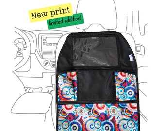 May include: Black car seat organizer with a clear plastic window and multiple pockets. The organizer has a colorful print of circles in shades of blue, red, orange, and white. The text "New print limited edition!" is on a yellow and green label.
