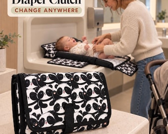May include: A rectangular diaper clutch featuring a black and white panda bear pattern with a black fabric trim and a central velcro closure tab. The text Diaper Clutch CHANGE ANYWHERE is visible in the upper left corner of the image.
