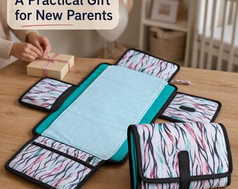 May include: A portable baby changing mat featuring a white fabric with a colorful abstract wavy pattern in shades of pink, teal, and black. The interior is light blue with a subtle white heart print. One unit is folded, and one is laid flat.