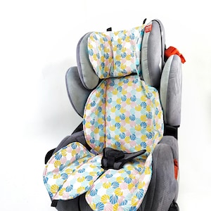 Puede incluir: Una silla de coche gris con un forro acolchado extraíble que presenta un patrón geométrico de abanicos en amarillo, azul y rosa. El asiento incluye alas de reposacabezas ajustables, una hebilla de arnés central y tela gris texturizada.